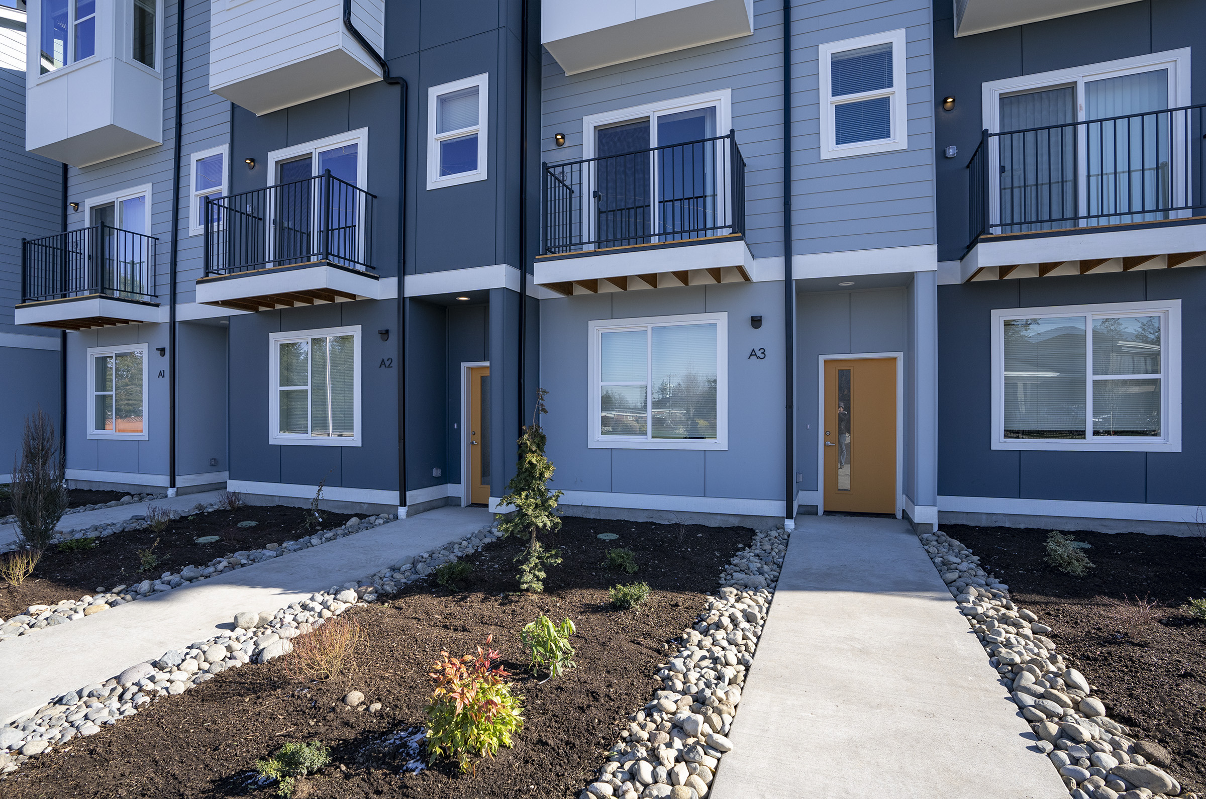 Front walkways and private entries with balconies and river-rock landscaping — One-12 Townhomes Lakewood WA